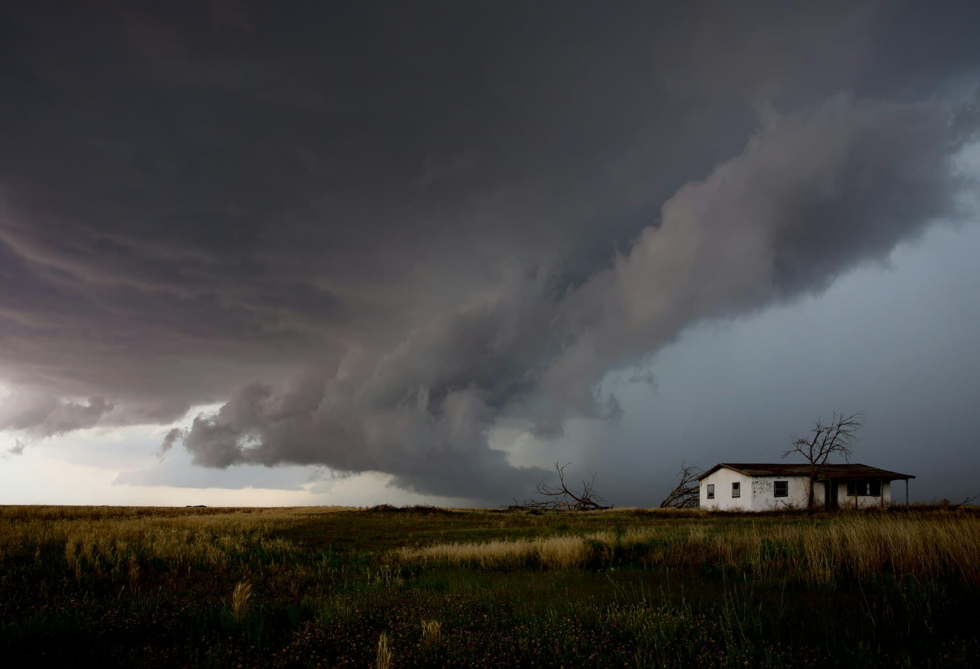 Dark supercell storm cloud rolling over a small Texas prairie farmhouse